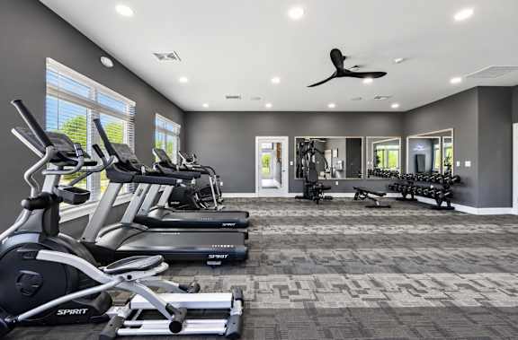 A spacious gym with treadmills, elliptical machines, and a fan.