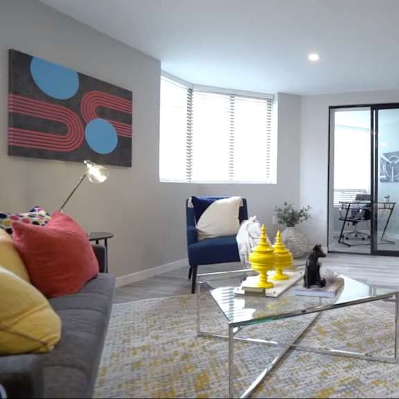 A living room with a glass coffee table and a yellow vase on it.