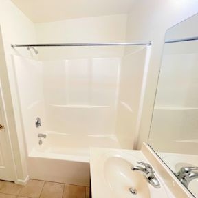 A white bathroom with a tub, sink, and mirror.