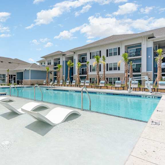 A large swimming pool in front of a building with palm trees.