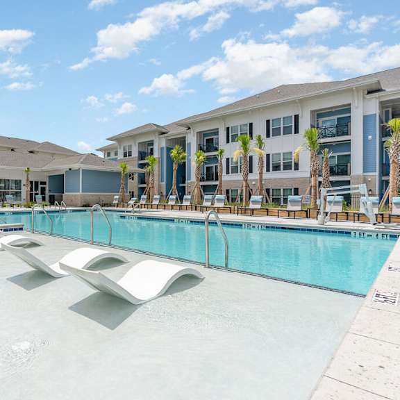 A large swimming pool in front of a building with palm trees. at The Banks at Bridgewater Apartments, South Carolina, 29566