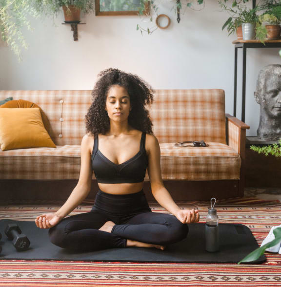 a woman sitting on a yoga mat in a living room with a couch