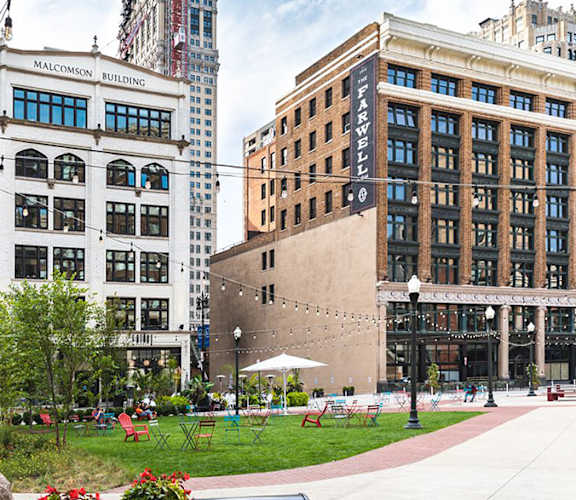 A city park with a large rock in the foreground and a building with a sign that says  at 28Grand, Detroit, MI