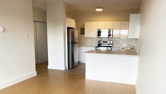 A modern kitchen with a stainless steel refrigerator and wooden flooring.