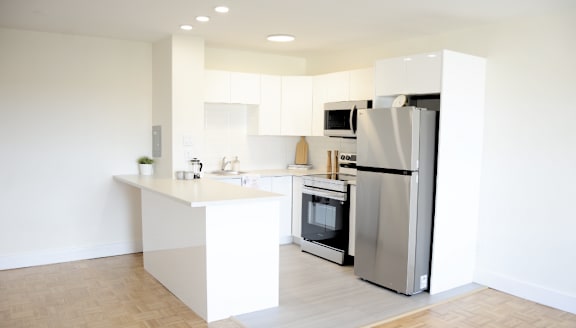 A modern kitchen with a stainless steel refrigerator and wooden flooring.