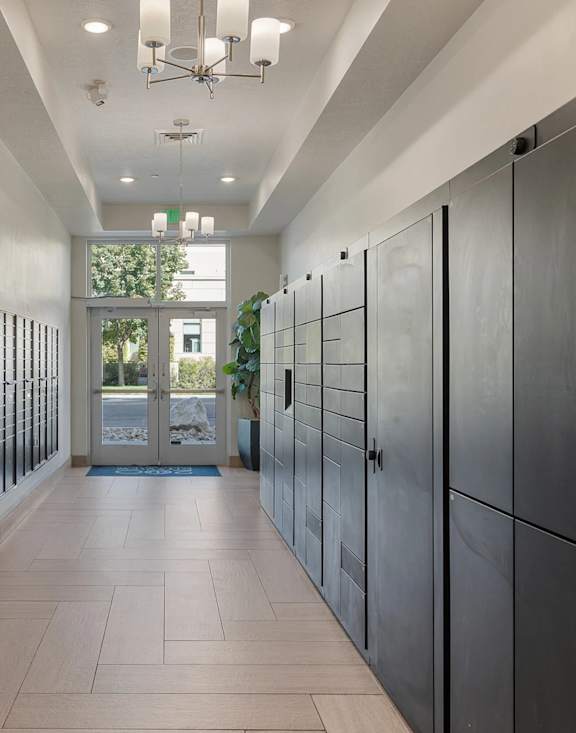 A hallway with a row of black lockers on the right and a door on the left.