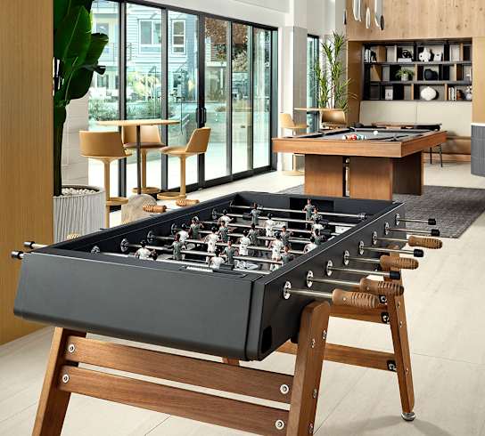 A foosball table is in the middle of a room with a lot of windows.