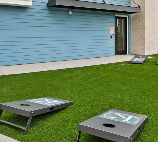 Two cornhole boards are on a green lawn in front of a blue house.