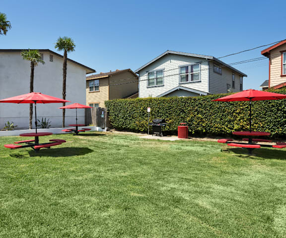 a backyard with picnic tables and umbrellas in front of houses