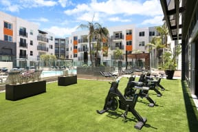 Outdoor fitness area with exercise machines on a lawn in front of an apartment building at Eleven 10.