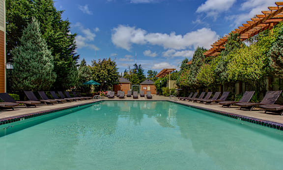 A large swimming pool surrounded by lounge chairs and trees at Commons at Sylvan Highlands Apartments, Oregon, 97225