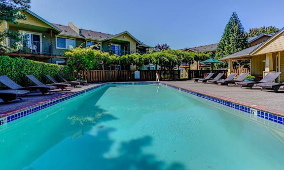 A swimming pool surrounded by lounge chairs and apartment buildings. at Commons at Hawthorn Village Apartments, Hillsboro, OR, 97124