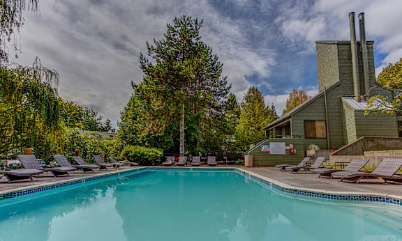 A large swimming pool surrounded by lounge chairs and trees at Commons at Redwood Creek Apartments, Beaverton, 97008
