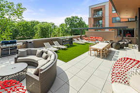 A roof-top terrace with a grilling station, fire pits, a comfortable seating area, chairs, tables, and lounge chairs on artificial turf. at Keva Flats, Exton, PA, 19341