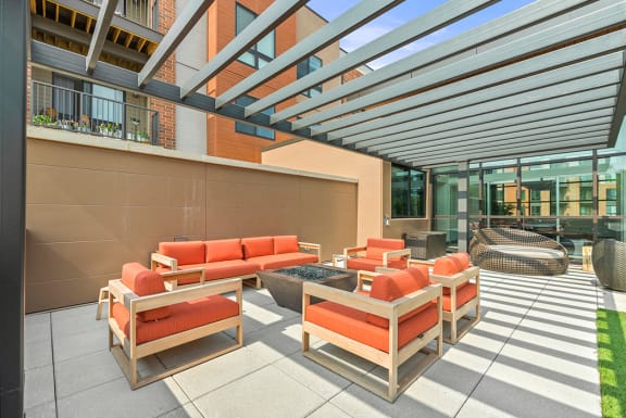 An outdoor patio with a fire pit, comfortable seating, large tile flooring, and artificial turf under a pergola. at Keva Flats, Exton, 19341