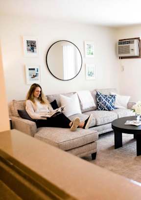 a woman sitting on a couch reading a book in a living room at Rosemont Place Apartments, Des Moines, IA, 50320