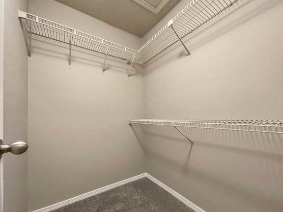 a walk in closet with a white wall and a hanging rack