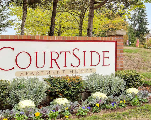 A sign that says "Courtside" in front of some trees.