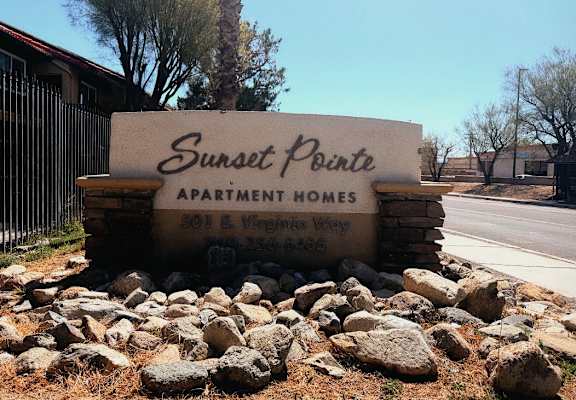 A sign for Sunset Pointe Apartment Homes sits in front of a fence and trees.