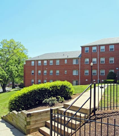 A red brick building with a black fence and a green lawn in front at Eagles Crossing Apartment, Washington, DC, 20032