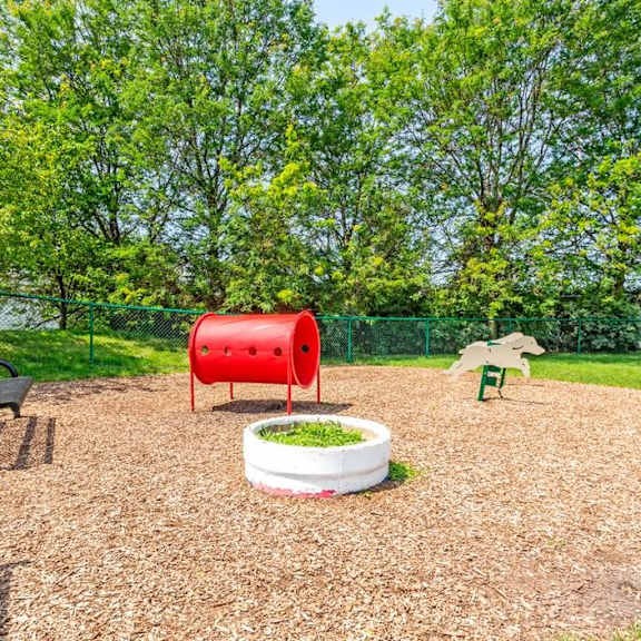 a fenced in play area with a red barrel and other playground equipment
