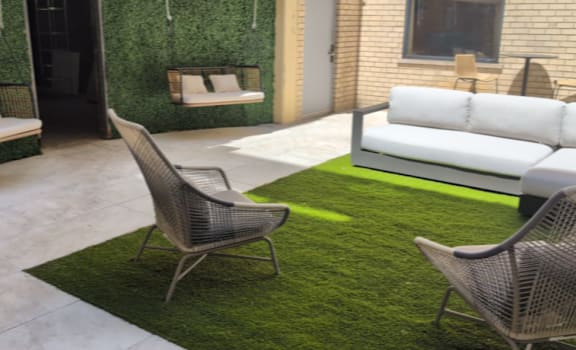 A patio with a white couch, a green rug, and a chair.