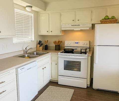 A white kitchen with a stove, sink, and refrigerator.