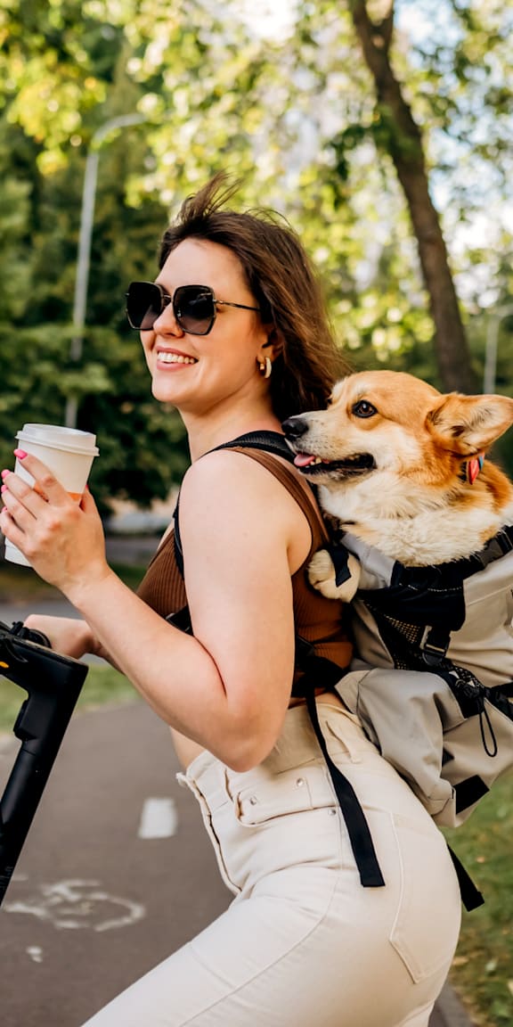 Woman Carrying Dog and Holding Coffee while Riding Scooter