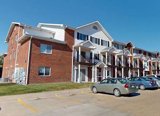 a red brick building with white pillars and siding in front of a parking lot