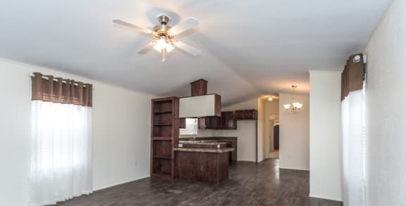 a living room with a ceiling fan and a kitchen in the background
