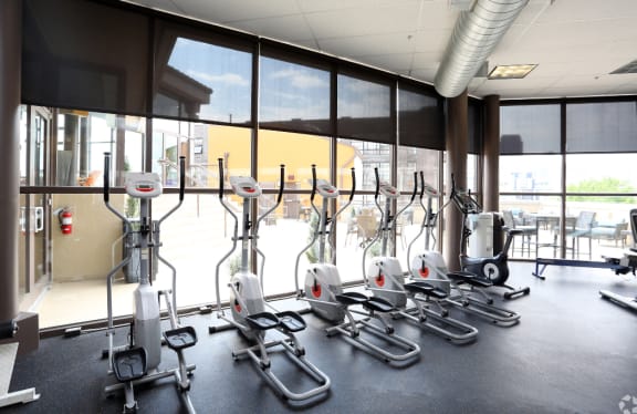 a fitness room with exercise equipment in front of windows