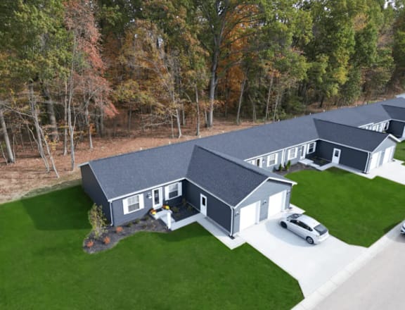 A large house with a grey roof is surrounded by a green lawn and trees.