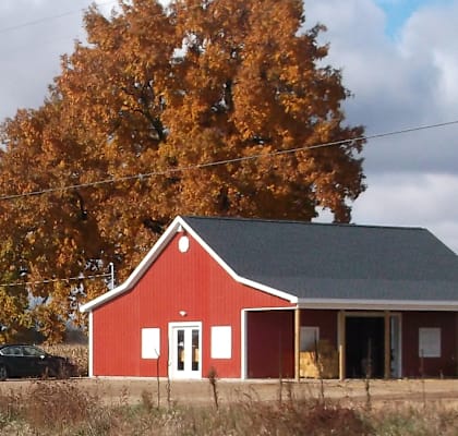 a red barn in front of a tree with orange leaves