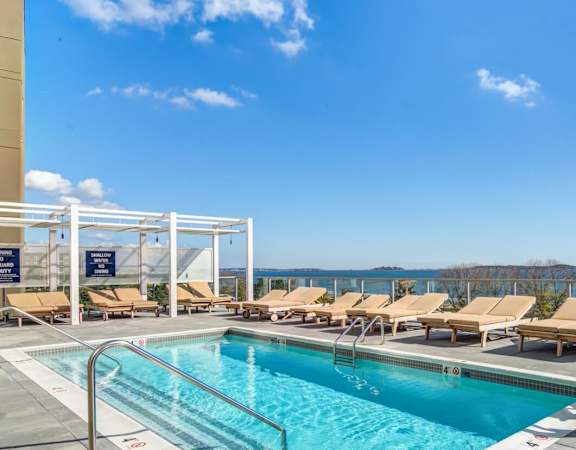 A large outdoor swimming pool with lounge chairs and a view of the water.