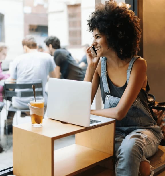 a woman sitting in a cafe talking on a cell phone while using a laptop computer at Heatherstone, Texas, 75287