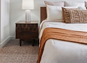Thumbnail 18 of 26 - A bed with a white comforter and a lamp on a side table.