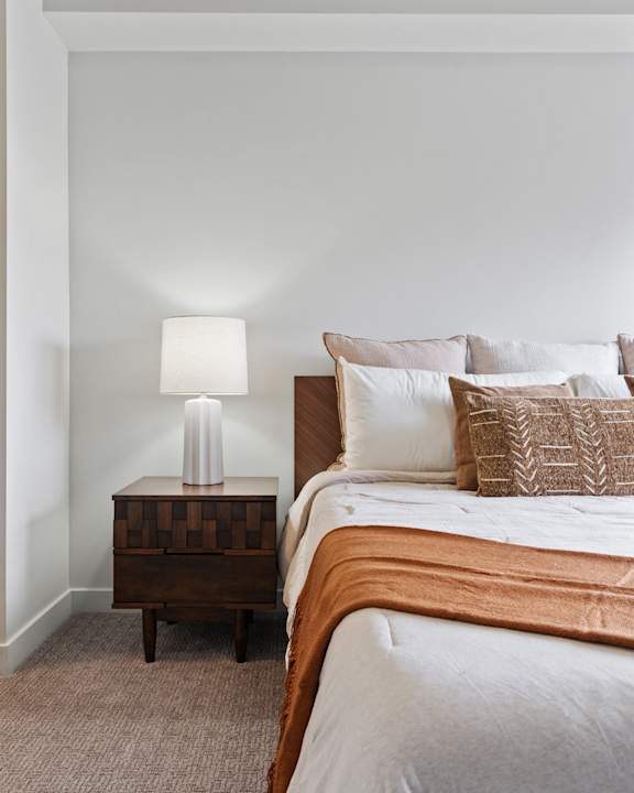 A bed with a white comforter and a lamp on a side table.