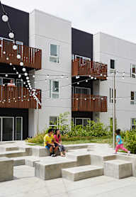 Two people sitting on a bench in front of a building with a balcony.