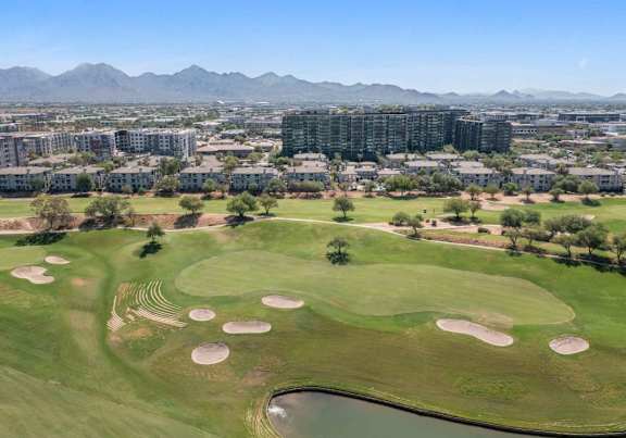 A golf course with a pond and sand traps in the foreground and apartment buildings in the background.