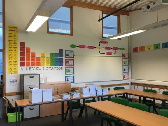 a classroom with desks and chairs and a bulletin board on the wall