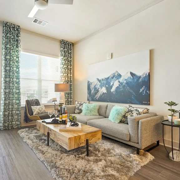 A living room with a grey couch, a wooden coffee table, and a large mountain painting on the wall.
