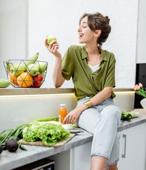 a woman sitting on a kitchen counter eating an apple