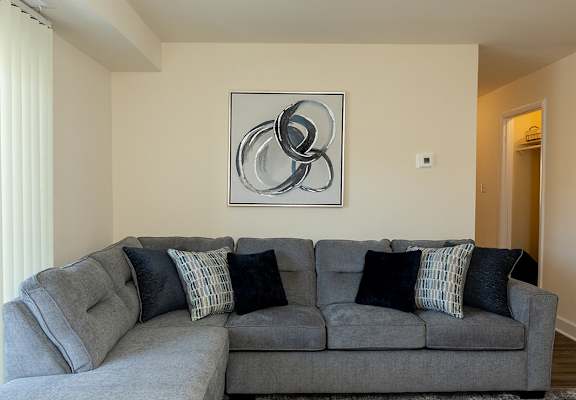 A grey couch with pillows and a large abstract painting on the wall.