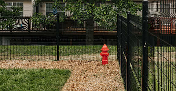 A red fire hydrant sits on a grassy area next to a black fence.