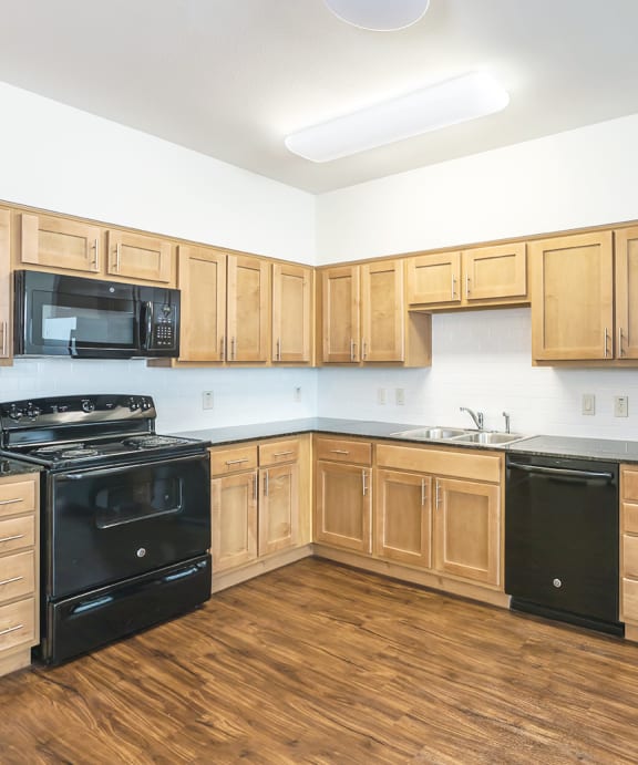 a kitchen with black appliances and wood shaker cabinets and hardwood flooring