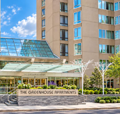 The Greenhouse Apartments building has a glass entrance and is surrounded by trees.