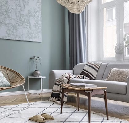 A living room with a grey couch, a wicker chair, and a small table with a plant on it.