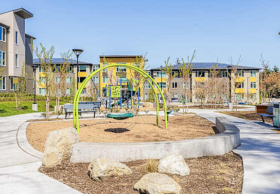 A playground with a yellow arch and a green slide in the middle of a park.