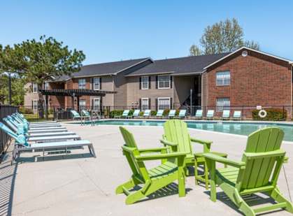A row of green Adirondack chairs are lined up by a pool.