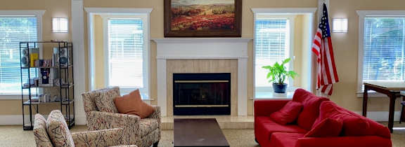 A living room with a fireplace, chairs, and a red couch.